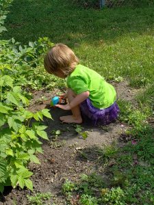 A little boy digging in the dirt in his sister's purple tutu.